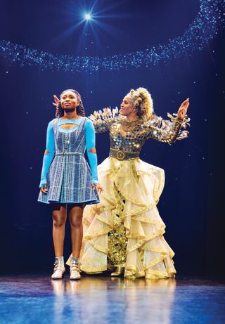 a girl (nichelle lewis as dorothy) stands on stage as a woman (deborah cox as glinda) stands to her right and sings to her, with a starry halo in the background
