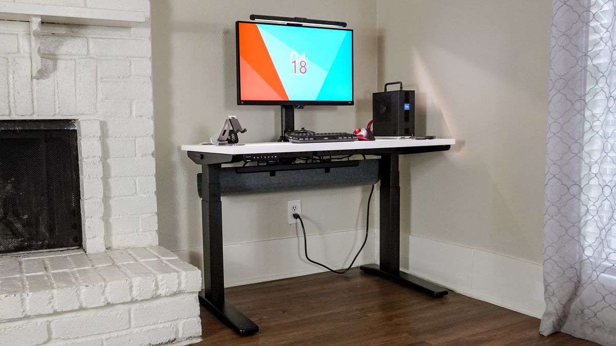 The Uplift V3 standing desk set up in a corner next to a fireplace