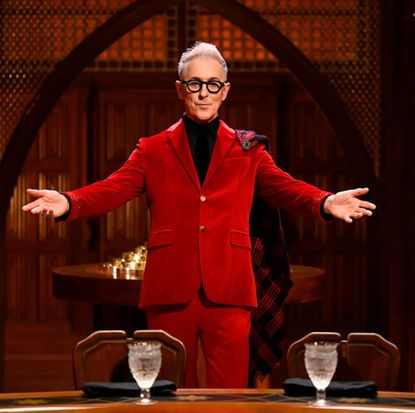 alan cumming poses with his arms outstretched in front of an empty round table, in 'the traitors' season 2