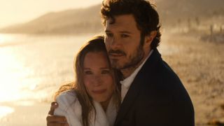 From left to right: Kristen Bell as Joanne and Adam Brody as Noah standing on a beach and hugging each other while looking forward in Nobody Wants This.