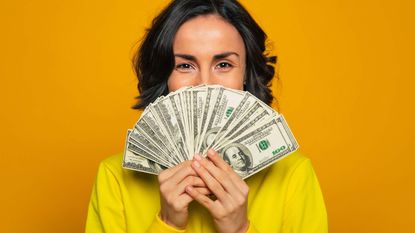 A woman holds a bunch of money like a fan in front of the bottom half of her face.