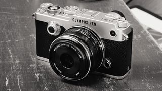 Olympus Pen-F digital rangefinder camera on a scratched wooden table