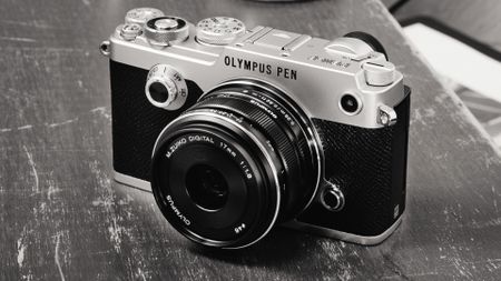 Olympus Pen-F digital rangefinder camera on a scratched wooden table