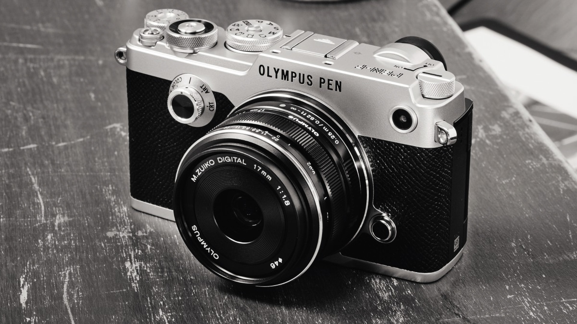 Olympus Pen-F digital rangefinder camera on a scratched wooden table