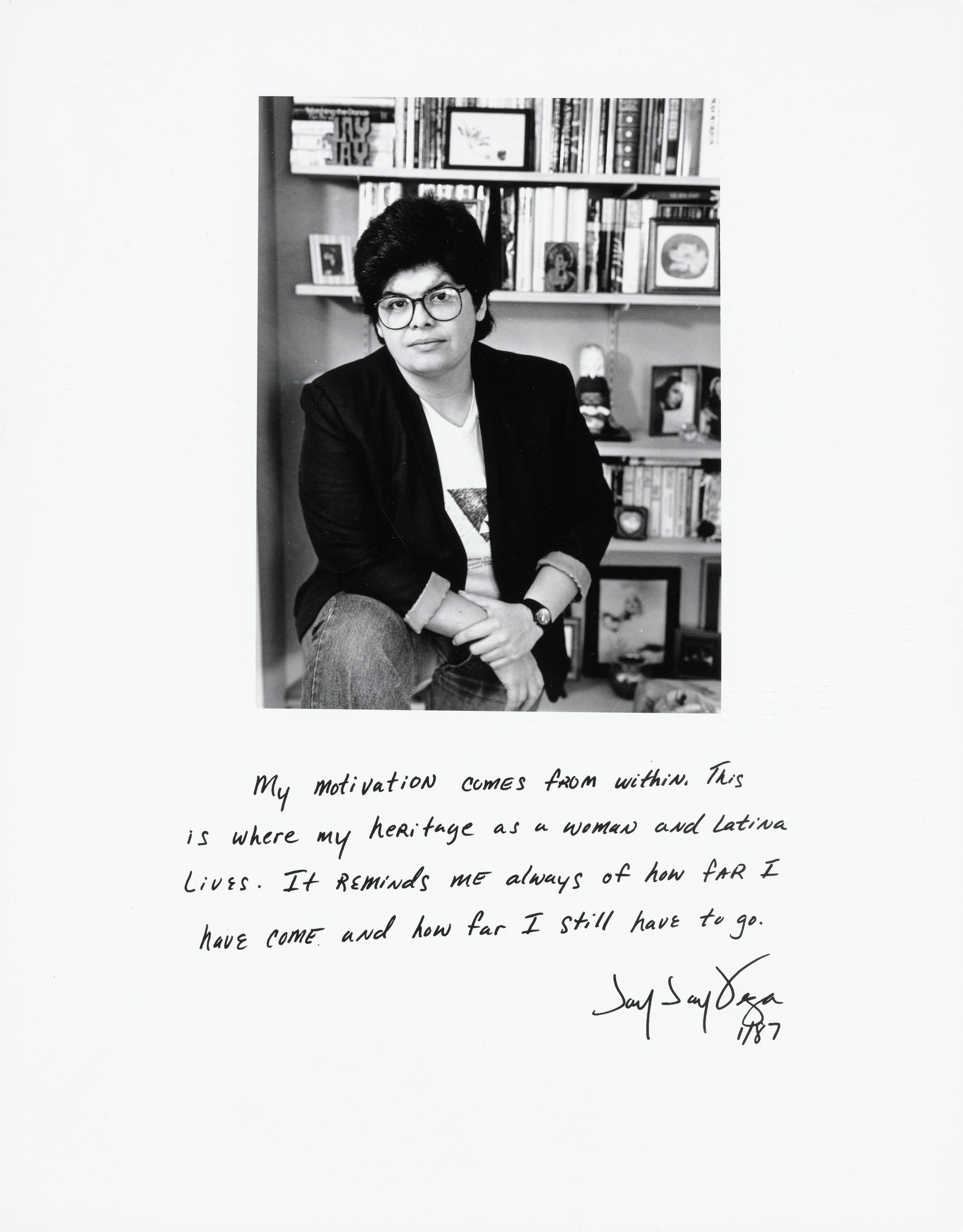 Black and white portrait of a woman with glasses seated in front of a bookshelf, with a handwritten personal statement and signature below the image.