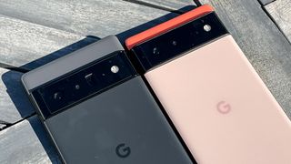 The Google Pixel 6 Pro (in black) and Google Pixel 6 (in coral) laid next to each other on wooden decking
