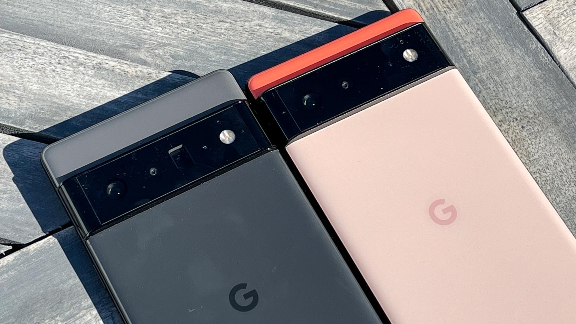 El Google Pixel 6 Pro (en negro) y el Google Pixel 6 (en coral) colocados uno al lado del otro en una terraza de madera