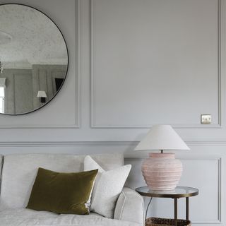 A living room with a panelled wall and a round antique-effect mirror hung above the cream sofa