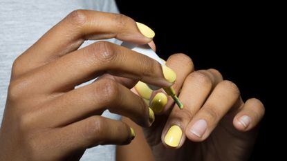 Close-up of woman applying nail varnish, with black background