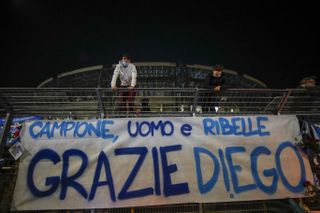 Supporters stand on fencing above a banner reading 'Champion, man, rebel, thank you Diego' placed outside the San Paolo in Naples