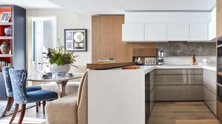 An example of small kitchen ideas showing a peninsula kitchen island with white cabinets next to a dining area with blue chairs