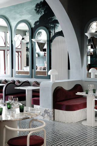 An art deco restaurant features mint green and red interiors including upholstered velvet banquettes, tiled floors, vaults, and glass lighting.