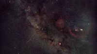 A photo of meteors streaking through a starry sky dotted with glowing nebulas and star clusters.