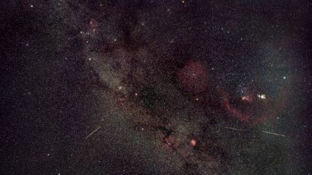 A photo of meteors streaking through a starry sky dotted with glowing nebulas and star clusters.