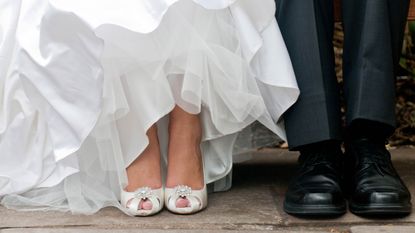 A bride and groom are seen from the knees down, in a white gown and black suit.