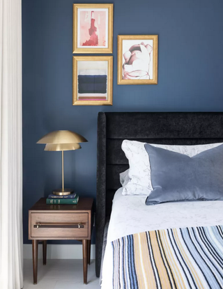 A blue bedroom with gold and white accents, including a statement table lamp and wall art