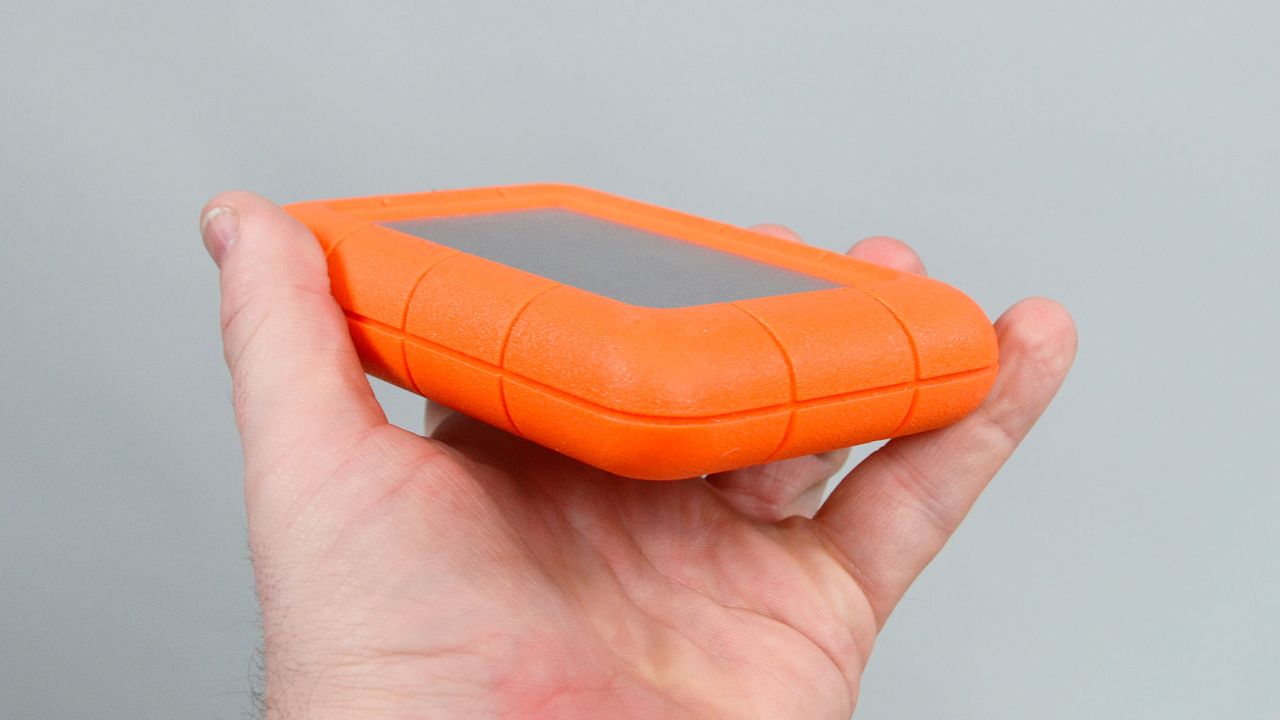 A masculine hand holding a LaCie Rugged Mini external hard drive