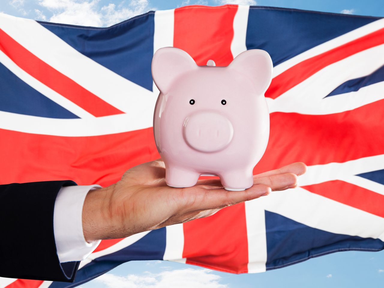 Businessman Holding Piggybank In Front Of British Flag