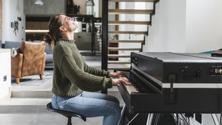 Smiling woman in green jumper sits at a piano
