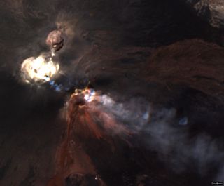 Smoke pours from the top of a volcano, as seen from orbit. Small rings of smoke are visible.