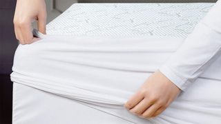 A pair of hands fitting the Utopia Bedding Bamboo Mattress Protector onto a bed