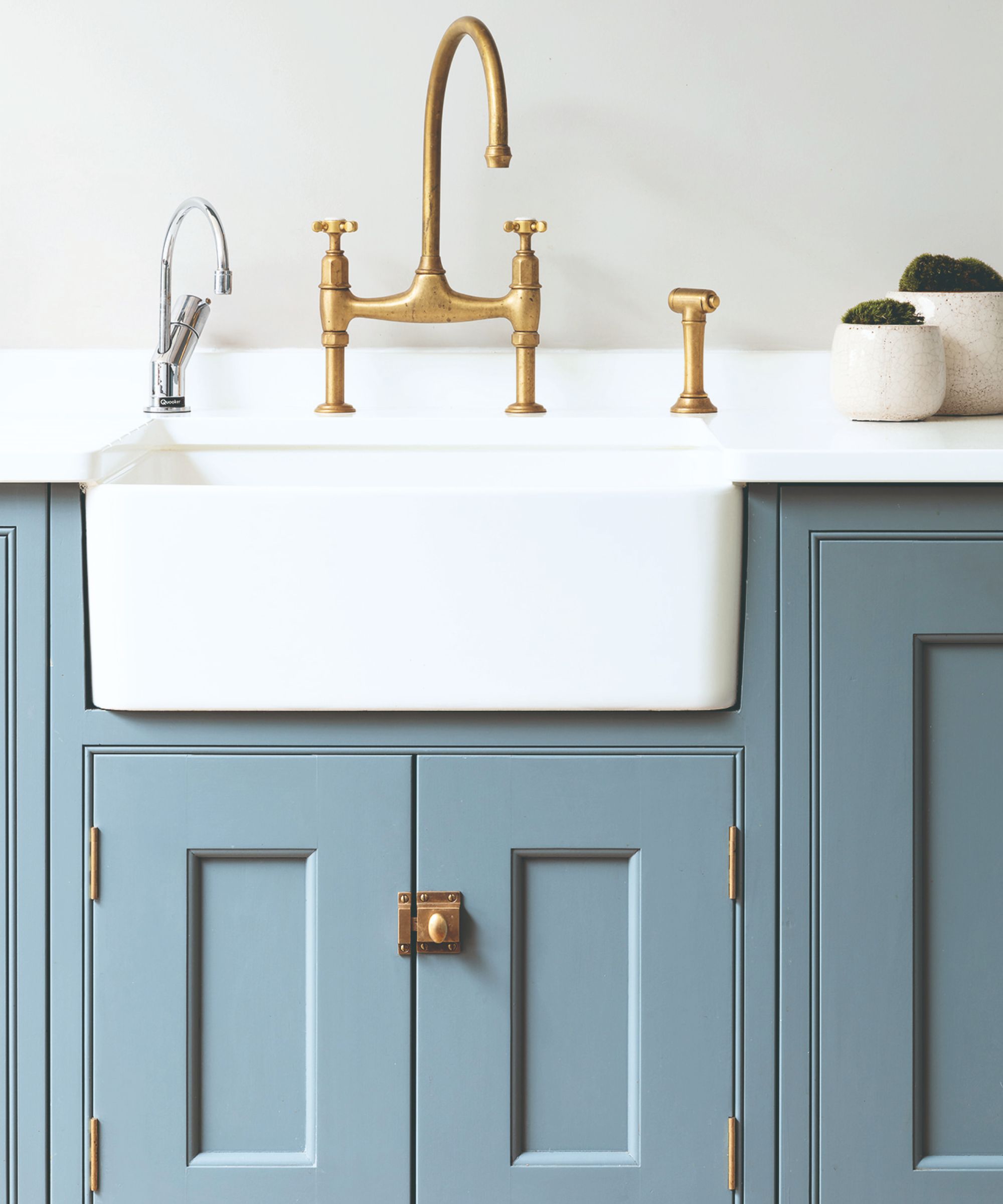 A kitchen ceramic kitchen sink with a tall brass faucet and blue cabinets