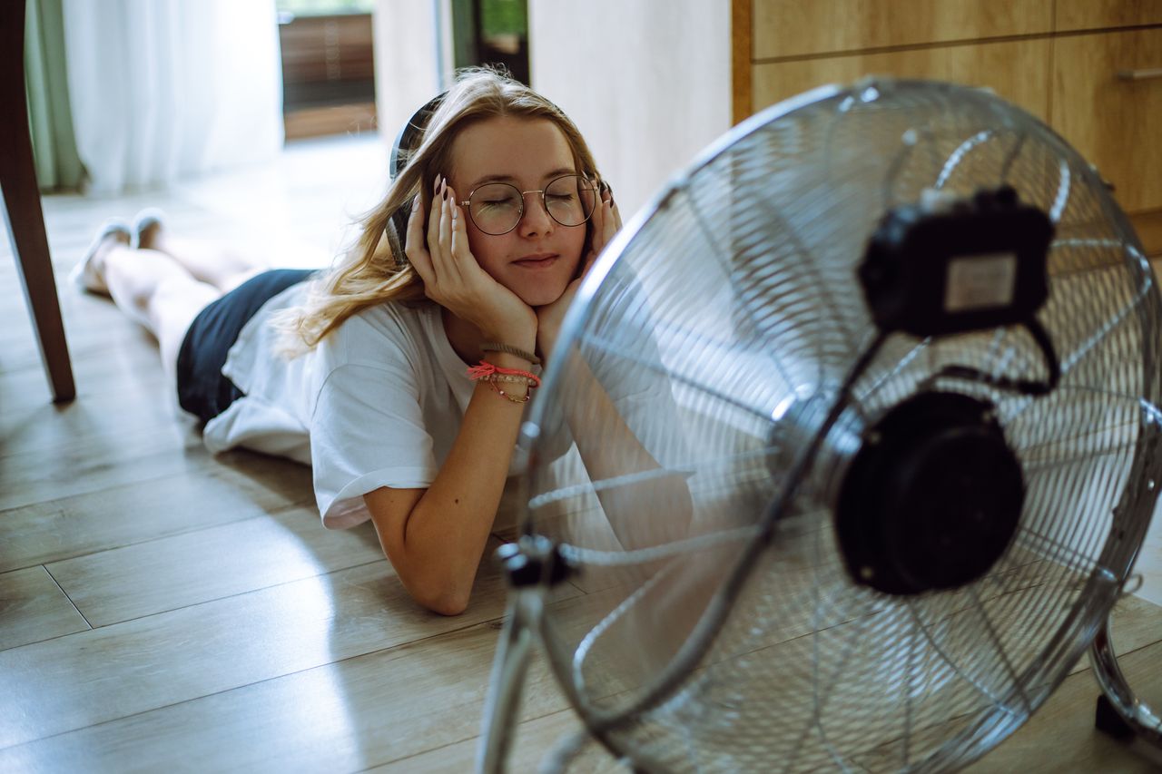 teen girl creates her personal oasis on the floor, listening to music through wireless headphones in front of a cooling fan