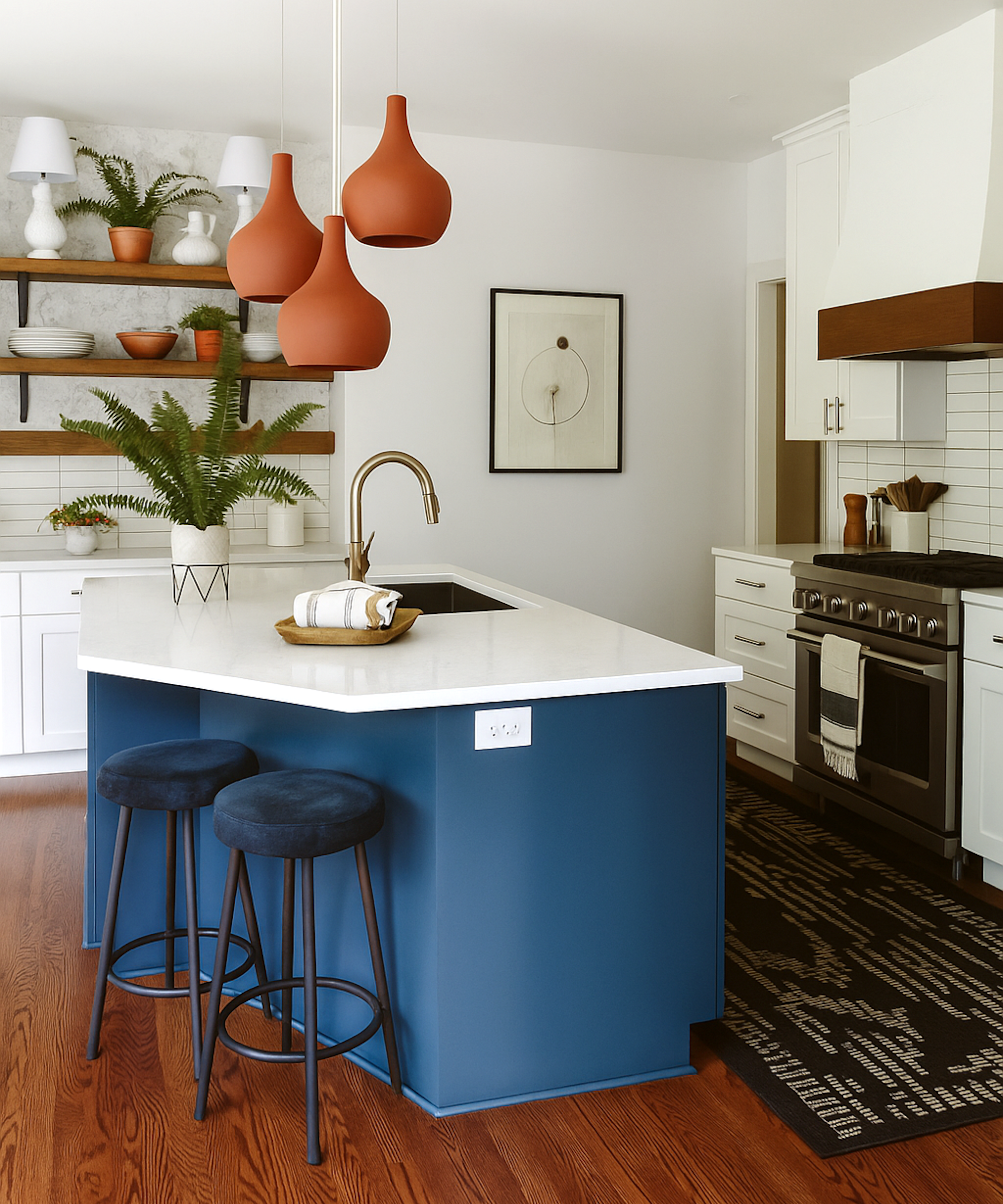 Kitchen with white cabinets and blue island, white countertops, wall shelves, pendant lights above island and two bar stools