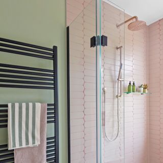 bathroom with shower with rose gold brassware, a glass shelf for shampoo bottles and pink tiles and a black towel radiator beside