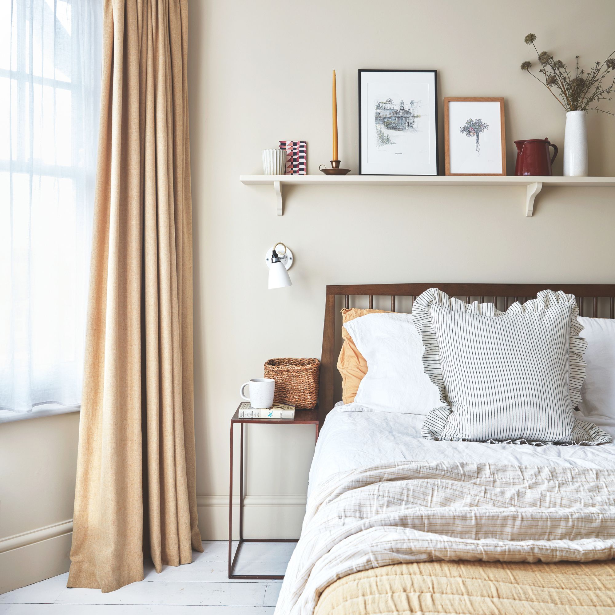 Neutral painted bedroom with cream curtains and white/cream bedding on the bed, with a shelf on the wall above it