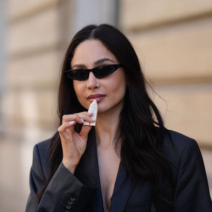 street style shot of woman in sunglasses applying lip balm