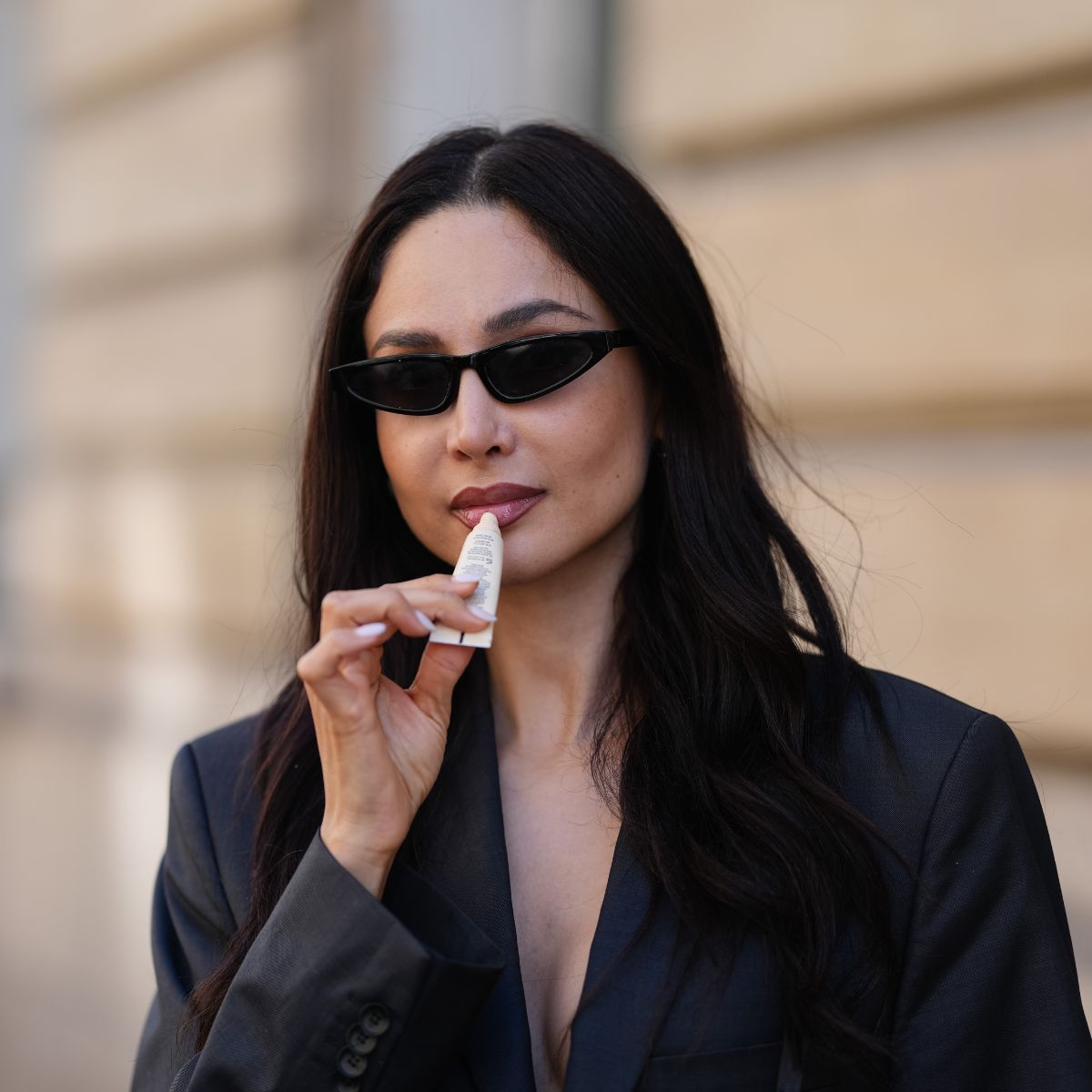 street style shot of woman in sunglasses applying lip balm
