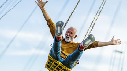 An older man spreads his arms wide as he swings through the air on an amusement park ride.