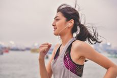 Woman Listening Music While Jogging By River Against Sky - two workouts a day