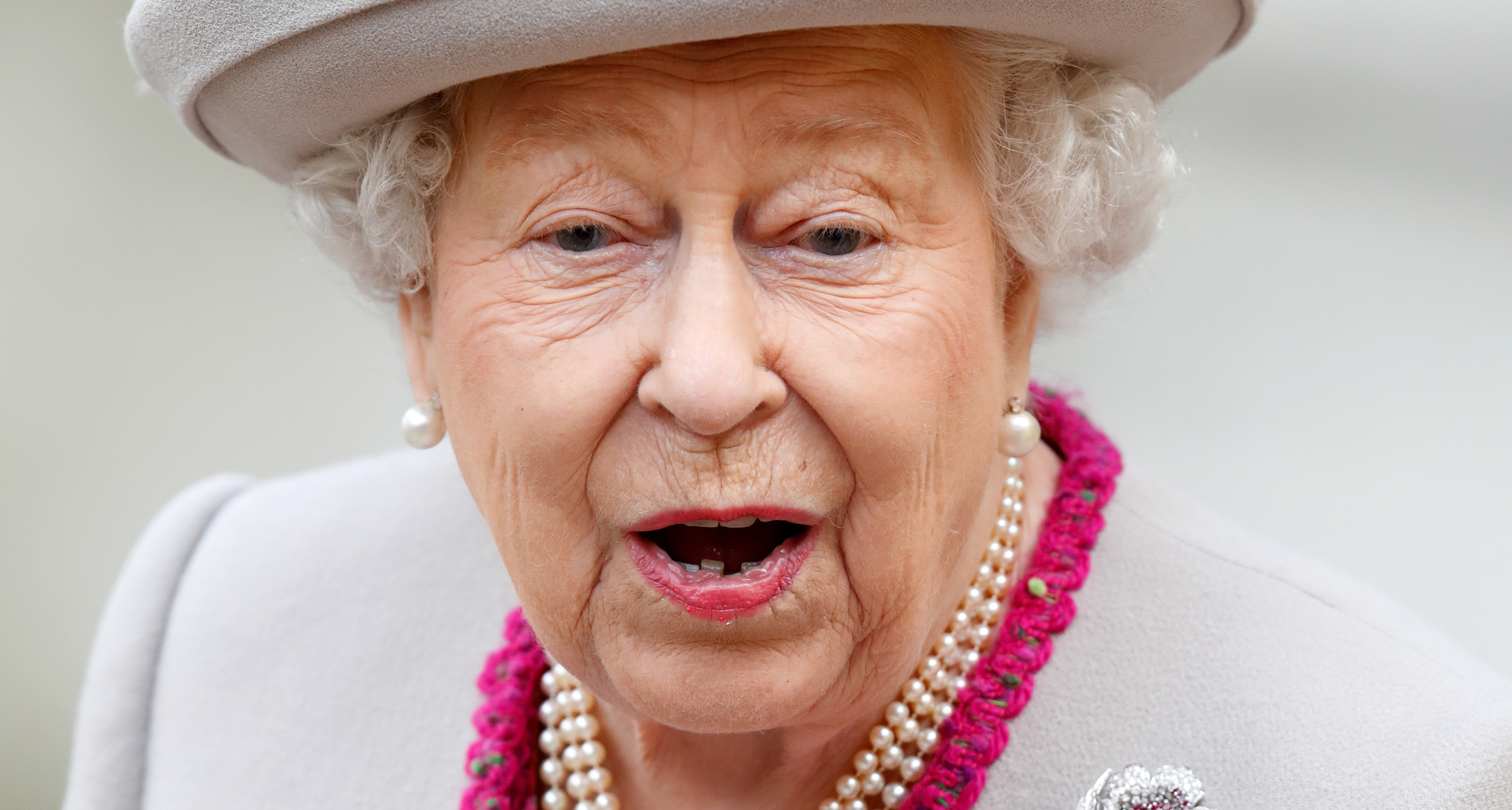 Queen Elizabeth making a shocked face wearing a gray hat and pearls
