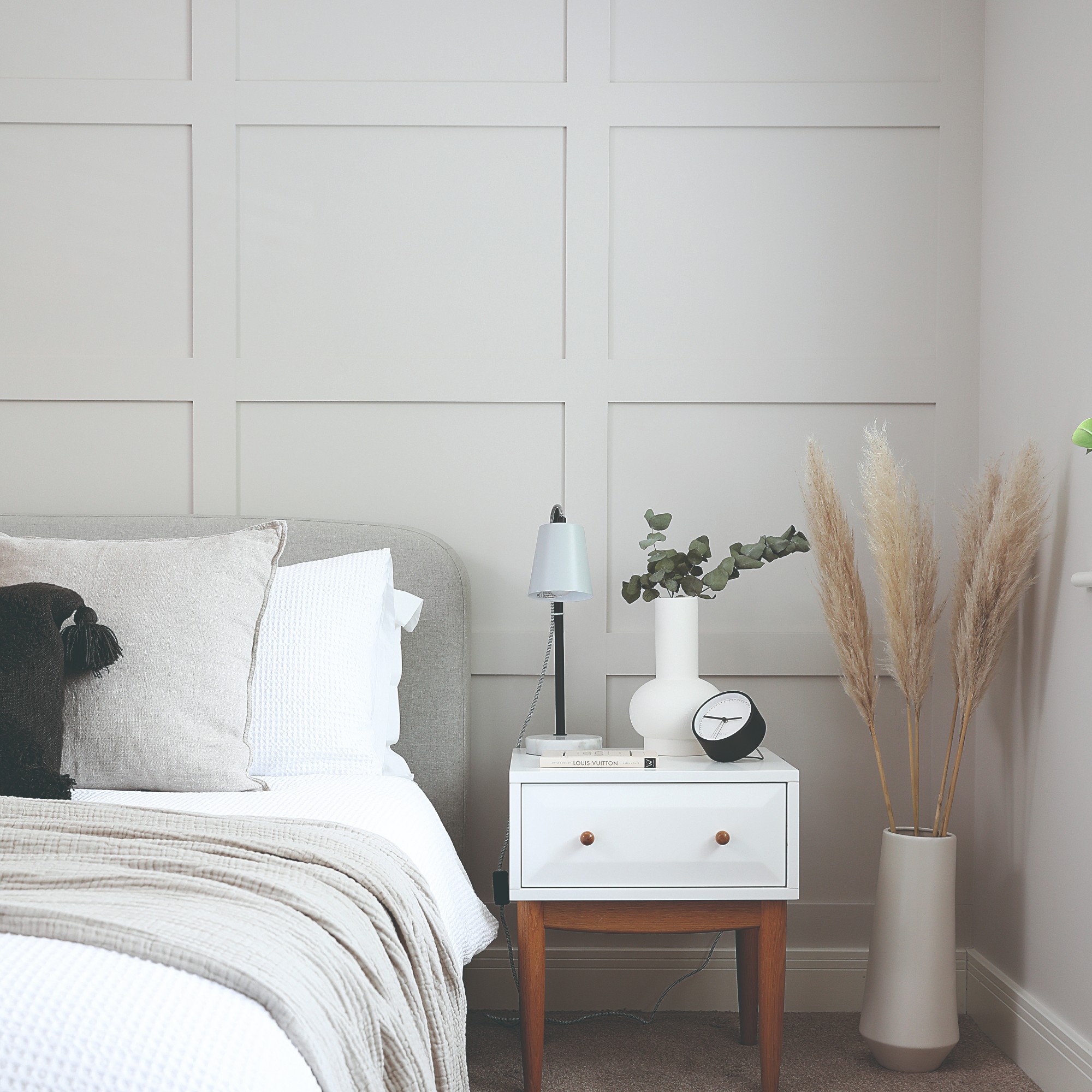 A white bedroom with a feature wall behind the bed covered in a panelling-effect wallpaper in off white