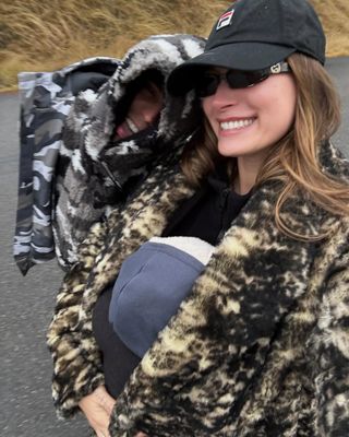 Hailey Bieber wearing black baseball cap and coat walking with baby.