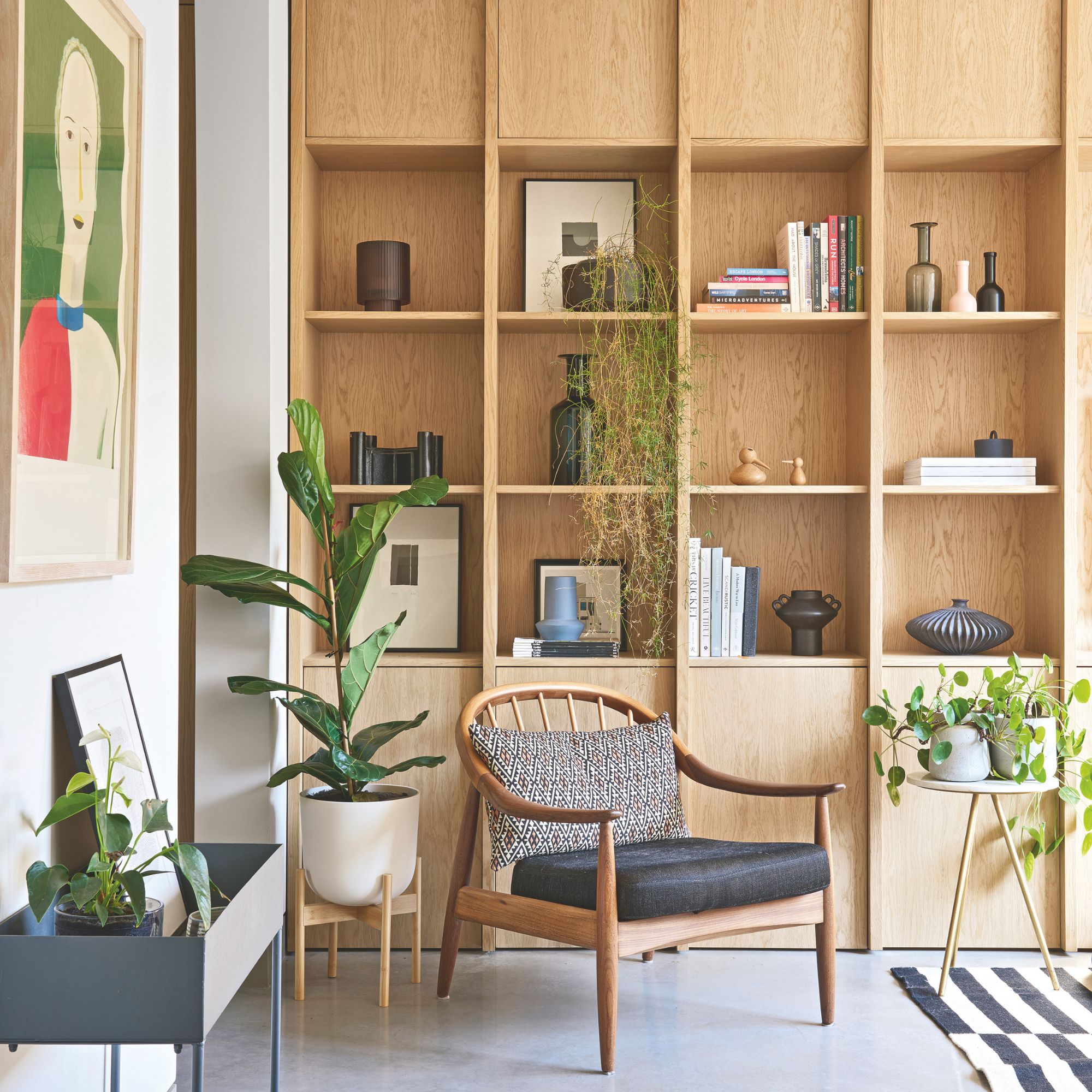 Wooden accent chair sitting in front of wooden shelving unit covered in plants and home decor