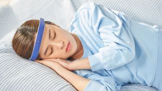 A woman sleeping on her side wearing the FRENZ Brainband and a blue jumper 