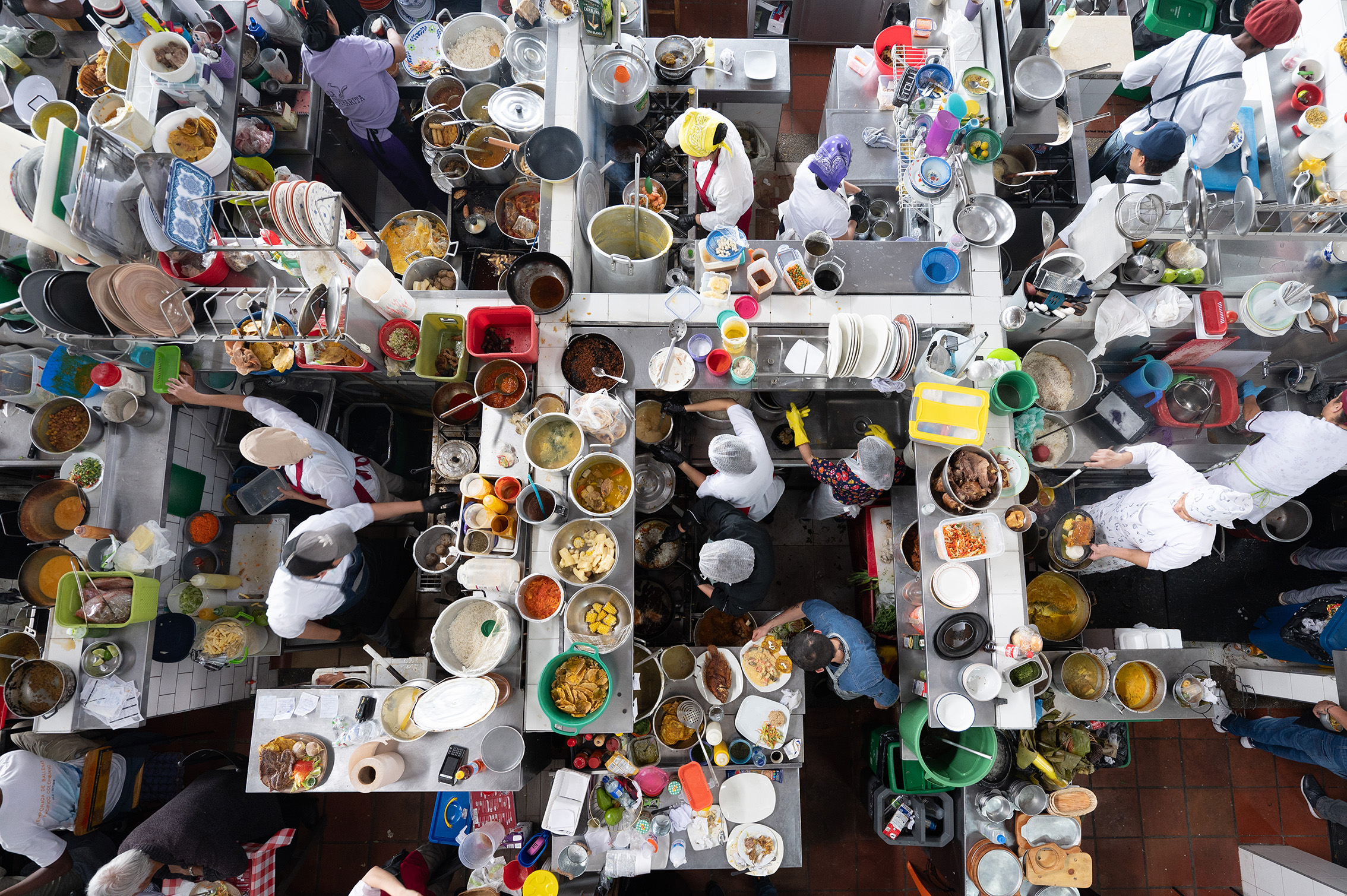 Aerial view of a bustling kitchen with chefs preparing various dishes. Counters are filled with colorful ingredients and steaming pots