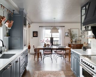 kitchen diner with navy cabinets. wooden floor, white range, wooden dining table, wood and metal chairs and white pendant