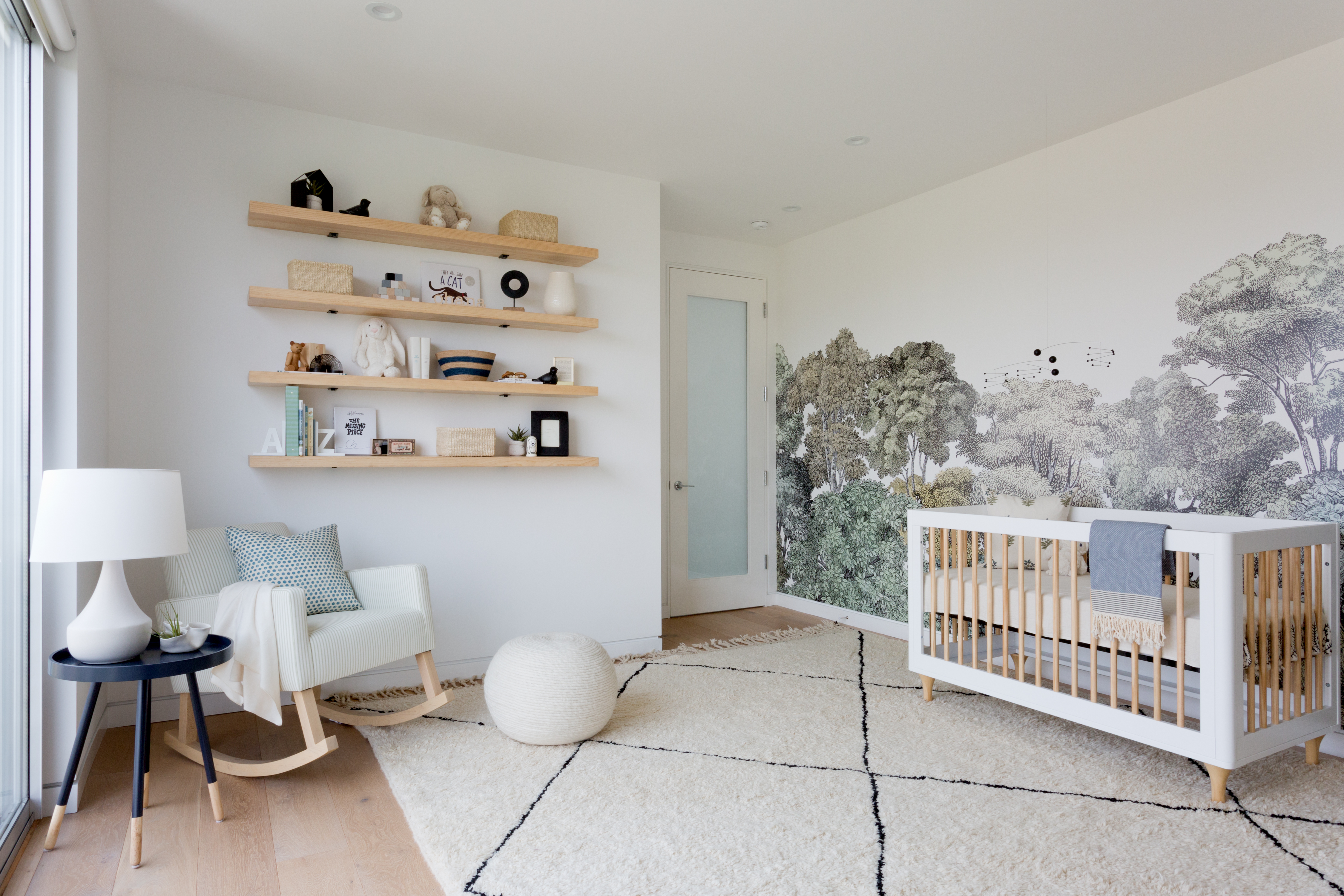 Nursery ideas in white, with open shelving and a tree mural on one wall, with white berber rug and neutral furniture.