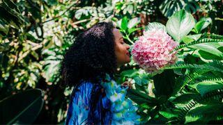 Woman sniffing a large flower at a botanical a garden with eyes closed