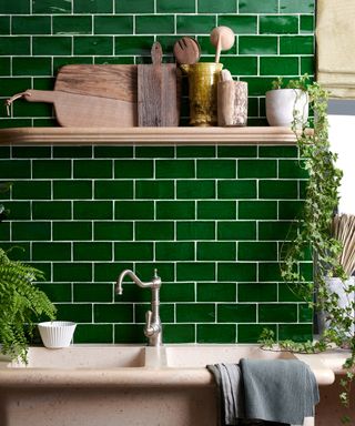 Dark green kitchen wall tile ideas creating a feature wall behind a large stone sink, with a single wooden shelf higher up the wall.