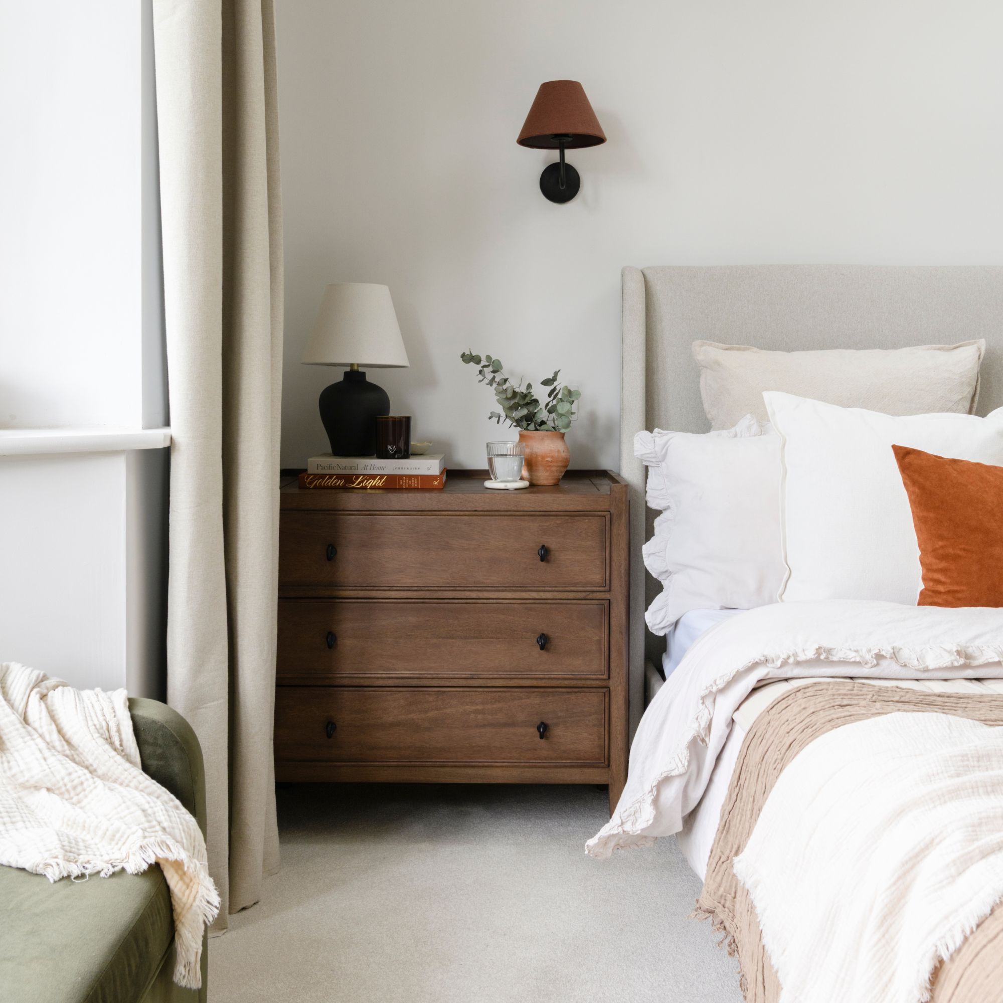 White painted bedroom with wooden chest of drawers next to the bed covered in plain white bedding