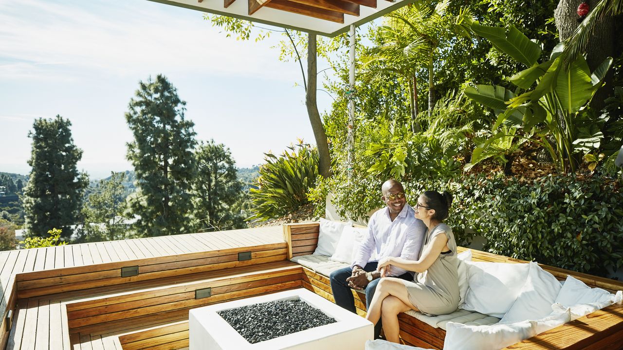 A couple sit next to each other at the fire pit of a clearly wealthy estate. 