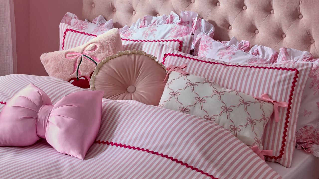 A pink bedroom with a striped bedding, a bow-shaped cushion and a cherry-embroidered cushion 