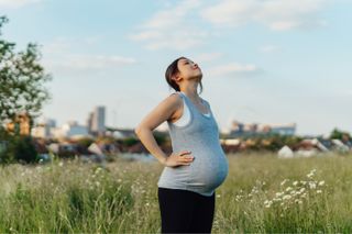 A young pregnant woman stood in a field breathing in fresh air