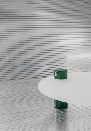 The deep green volume in a round shape supports the white round tabletop and emerges on top of it.