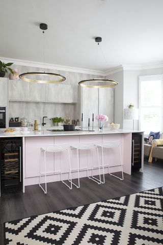 Kitchen with concrete-effect wall units, light pink island, white metal bar stools, dark wood floor, monochrome geometric rug and statement circular pendant lights